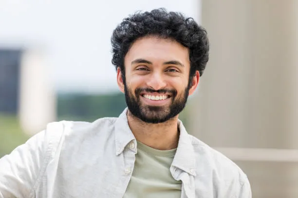 The young adult male student teacher stands outside and smiles for the camera to update his headshot photo.